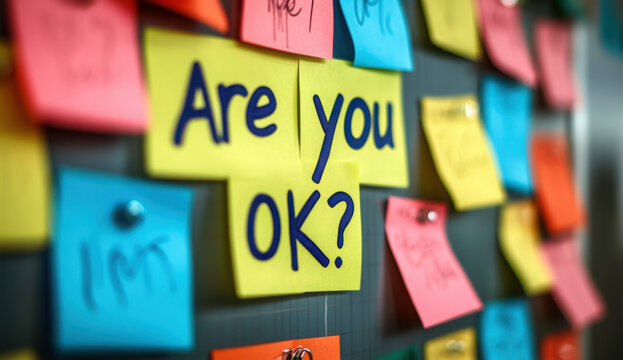 Colorful sticky notes on corkboard. One note says Okay Workplace mental health initiative. Employee support. Caring, encouraging work environment. Positive message for colleagues. Promoting