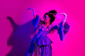 Elegant woman in baroque-style costume and neon lighting expressing joy in a modern historical...