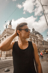 handsome man of European appearance in glasses in summer in Ukraine in the city of Lviv during travel and vacation. Opera house and historical landmark