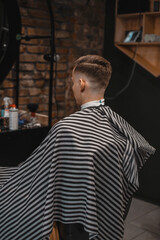 A barber man with a tattoo on his arm makes a haircut to a brunette guy in a barbershop, cuts his hair with a clipper close-up