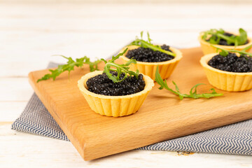 Tartlets with black caviar served on on wooden table