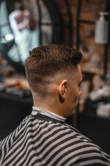 A barber man with a tattoo on his arm makes a haircut to a brunette guy in a barbershop, cuts his hair with a clipper close-up