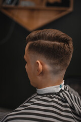 A barber man with a tattoo on his arm makes a haircut to a brunette guy in a barbershop, cuts his hair with a clipper close-up