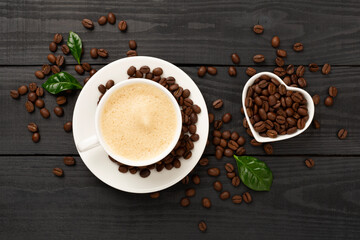 Cup of coffee with coffee beans and leaves on wooden background,top view