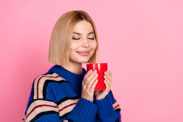 Young woman smiling with a red mug against a pink background, wearing a stylish striped sweater for...