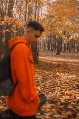 young man skater teenager in bright orange robe sitting outdoors in nature. Skateboarding in free time as a hobby. Beautiful autumn with orange leaves