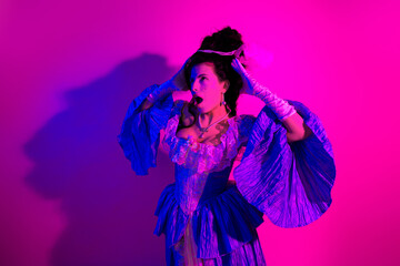 Elegant young woman in a historic royal costume under vibrant ultraviolet lighting with pink tones