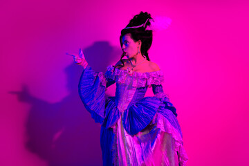 Elegant woman in vintage royal costume posing against a vibrant neon pink backdrop