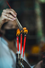 Naklejka premium Hand Lighting Red Incense Sticks in a Temple Ritual, Close-Up of Spiritual Practice at a shrine