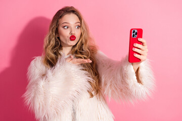 Stylish woman in white fur coat taking selfie against pink background