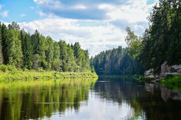 Obraz premium The Gauja River in the historic landscape of Livonia in Latvia, with picturesque reflections in the water, green trees in the background, and a wide summer sky, Latvia