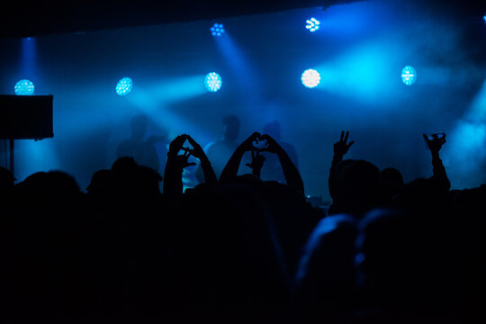 Crowd enjoying an indoors music festival performance while making heart signs with hands