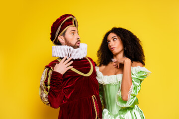 Costumed couple portraying historical aristocrats in vibrant attire against a yellow background,...