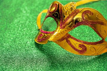 Golden carnival mask on green shiny background. Mardi Gras concept. Fat Tuesday symbol close-up.