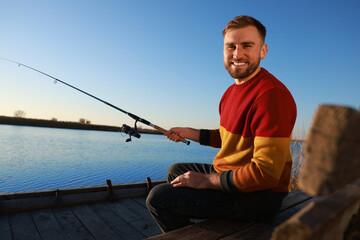 Fisherman with fishing rod at riverside on sunny day