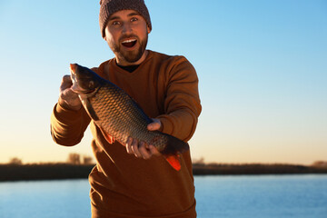 Fisherman holding caught fish at riverside. Recreational activity