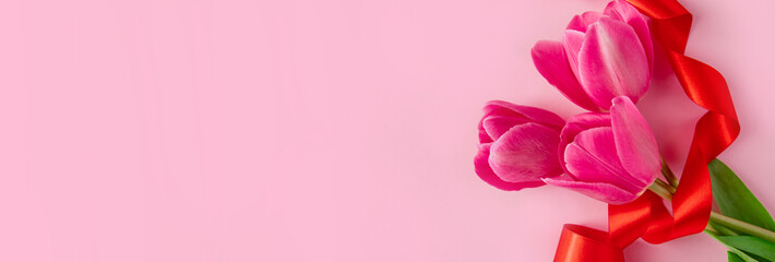 Fototapeta premium Bouquet of colorful fresh tulips with red ribbon on pink background. Symbol of spring. Happy easter.