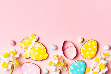 Easter-themed cookies in the shape of eggs and a bunny. Decorated with pastel icing and polka dots. Placed on a pink background with flowers and candy eggs. Festive spring composition.