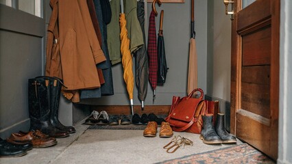 Entryway with organized coats, hats, and shoes on a vintage rug and wooden floor, evoking a rustic and inviting atmosphere