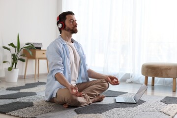 Man in headphones meditating near laptop on floor at home
