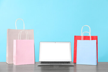 Internet shopping. Laptop and colorful paper bags on wooden table against light blue background