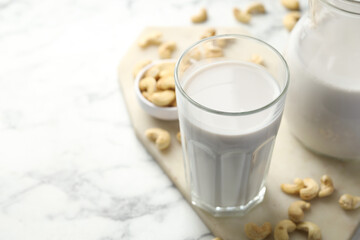 Fresh cashew milk in glass and nuts on white marble table, closeup. Space for text