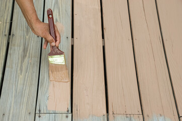 handyman painting the wooden deck with brush