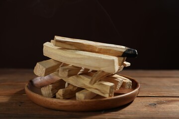Palo santo sticks and burnt one on wooden table against black background, closeup