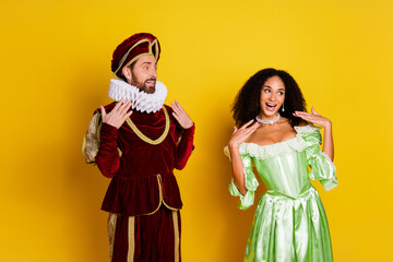Young couple in elegant vintage costumes posing cheerfully against a vibrant yellow background