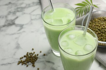 Fresh mung bean juice in glasses, seeds and twig on white marble table, closeup. Space for text