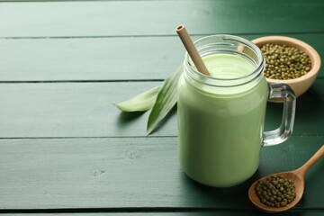 Fresh mung bean juice in mason jar, seeds and leaves on green wooden table, closeup. Space for text