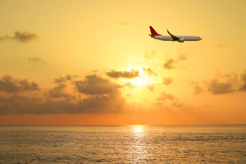 Airplane flying in sky over sea at sunset