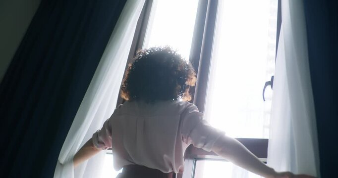 Beautiful Young Curly Hair Brunette Opens Curtains To let Morning Sunlight Illuminate Her Cozy Apartment, She Proceeds Dancing Beautifully and Quite.