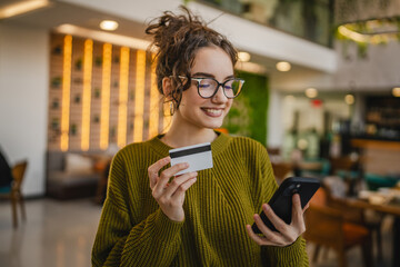 young woman use credit card for online shopping on cellphone at cafe