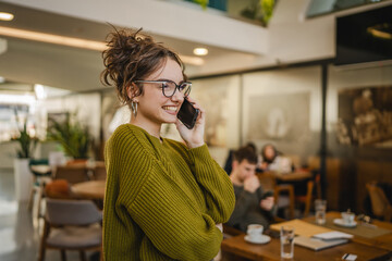young happy woman student standing in a cafe and talk on mobile phone