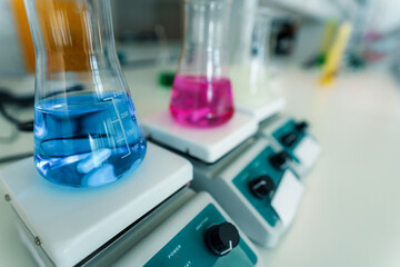 Flasks containing colorful chemical solutions are placed on laboratory hot plates, facilitating precise temperature control for experiments or reactions