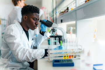 Focused young scientist using microscope, analyzing samples in test tubes, conducting research in a...