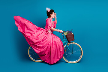 Full length photo of gorgeous pretty lady dressed pompous rococo costume driving cycle curious looking far empty space isolated blue color background