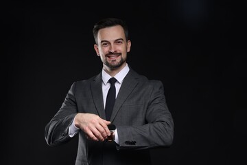 Handsome man in classic suit checking time on black background