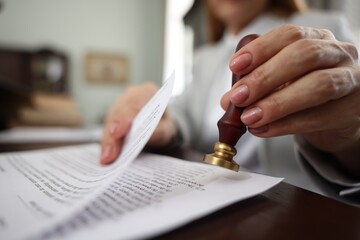 Notary stamping document at table in office, selective focus