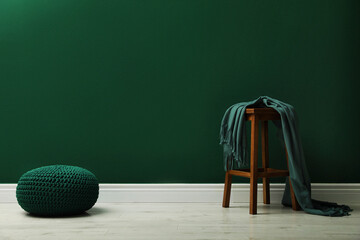 Stylish knitted pouf and wooden stool with blanket near green wall indoors, space for text