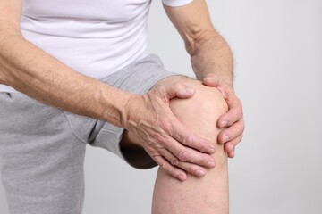 Senior man suffering from knee pain on light grey background, closeup