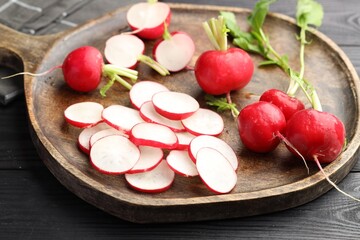 Fresh whole and cut radishes on black wooden table, closeup