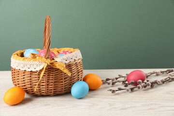 Many decorated Easter eggs in wicker basket and willow branches on wooden table against green...
