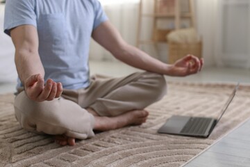 Man meditating near laptop on floor at home, closeup