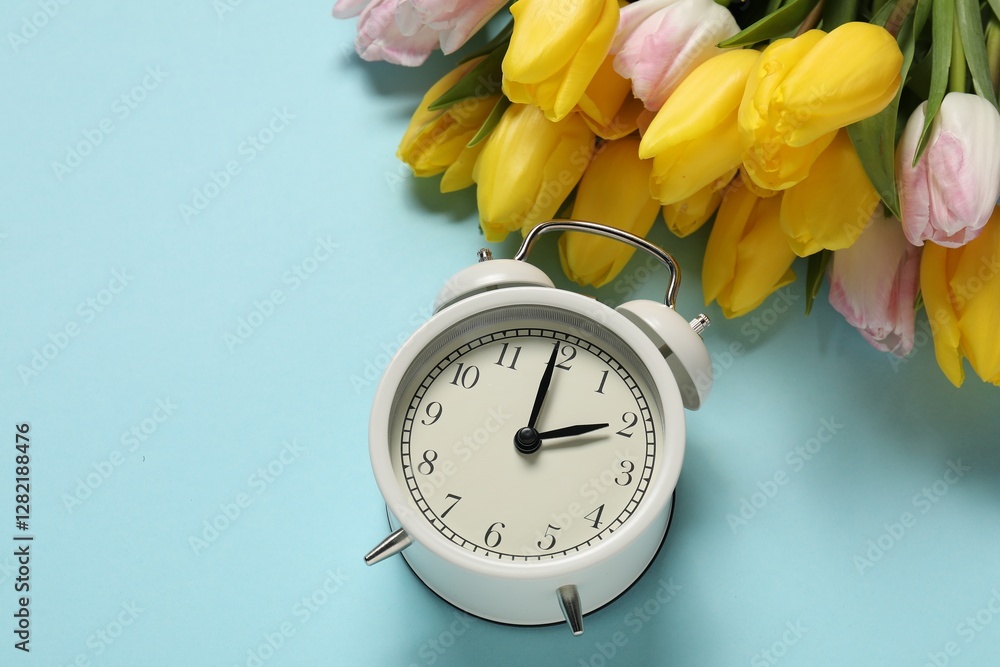 Poster spring time. alarm clock and beautiful tulips on light blue background, above view. space for text