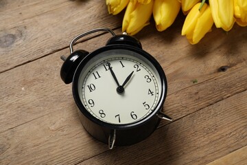 Spring time. Alarm clock and beautiful tulips on wooden table, above view