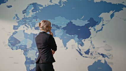 Thoughtful employee analyzing world map back view. Businesswoman brainstorming