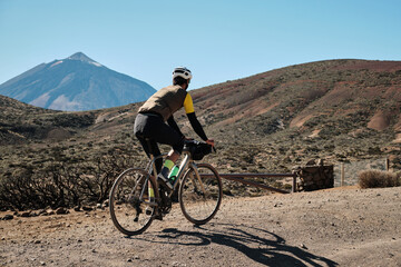 Cyclist enjoys a scenic ride through a volcanic landscape, with a majestic mountain in the background.  A stunning display of nature and adventure.