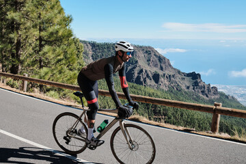 Fototapeta premium Cyclist on a scenic mountain road overlooking the ocean. Stunning landscape and active lifestyle photography. Perfect for travel, sports, or active lifestyle projects.